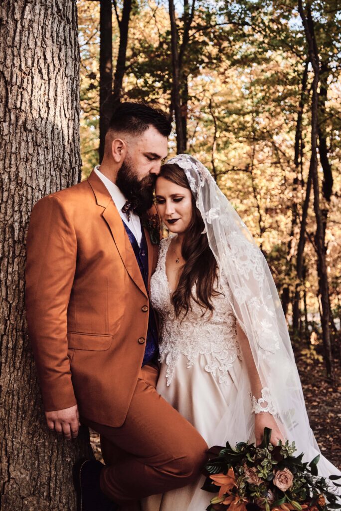 Wedding couple stands in trees together in the fall in Rochester Hills, Michigan