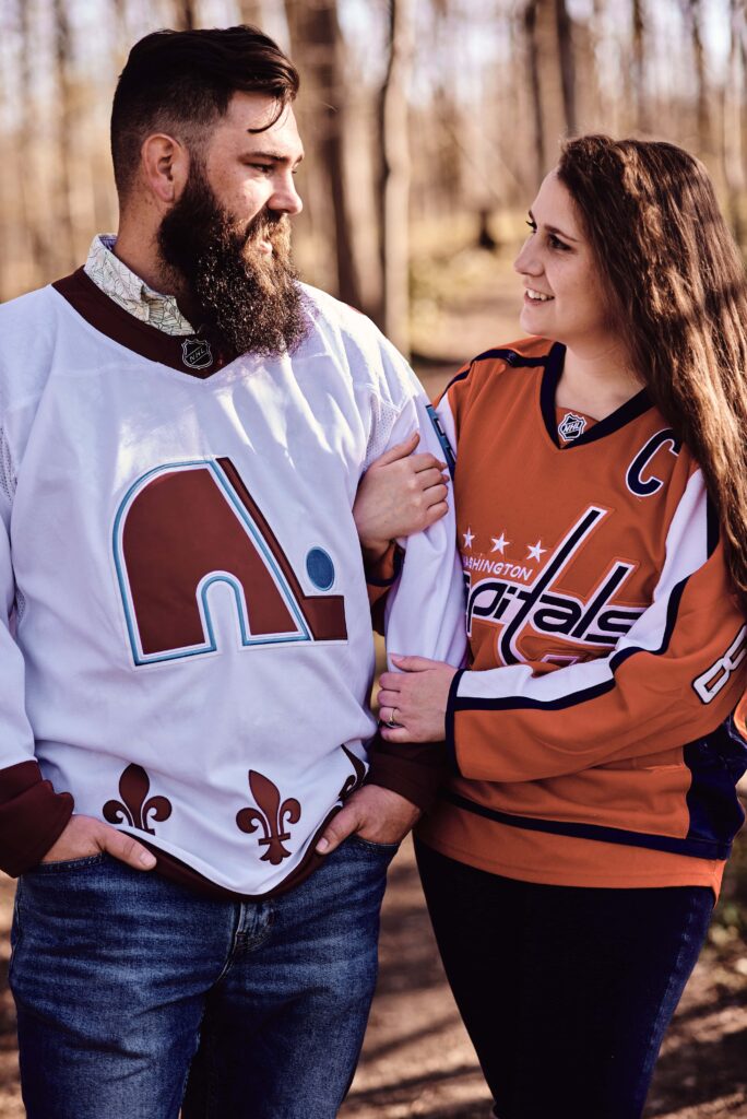 Couple looking at each other and embracing during their engagement session wearing their favorite NHL teams' jerseys. The location is Wolcott Mill Metropark in Ray Township, Michigan.