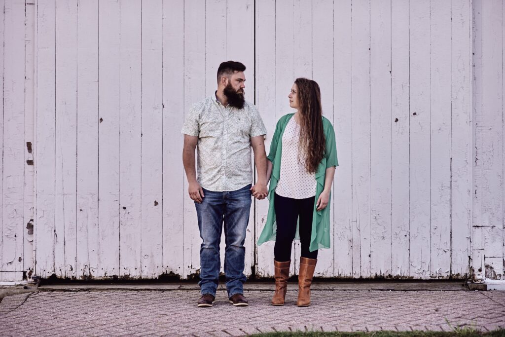 Couple standing in front of a white barn at Wolcott Mill Metropark in Ray Township, Michigan. One of the perfect Metro Detroit engagement session locations. Taken by Erika Black Photography