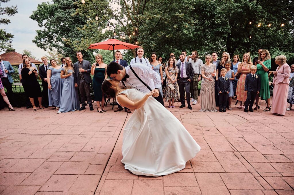 Bride and Groom dance their first dance. Groom dipping the bride while guests look on on the back patio outside of Pine Knob Mansion in Clarkston, MI. Photo taken by Erika Black Photography