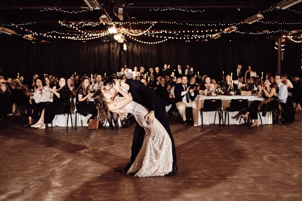 Groom dips and kisses bride in front of their guests during their first dance at the Royal Oak Farmer's Market in Royal Oak, MI. Photo taken by Erika Black Photography