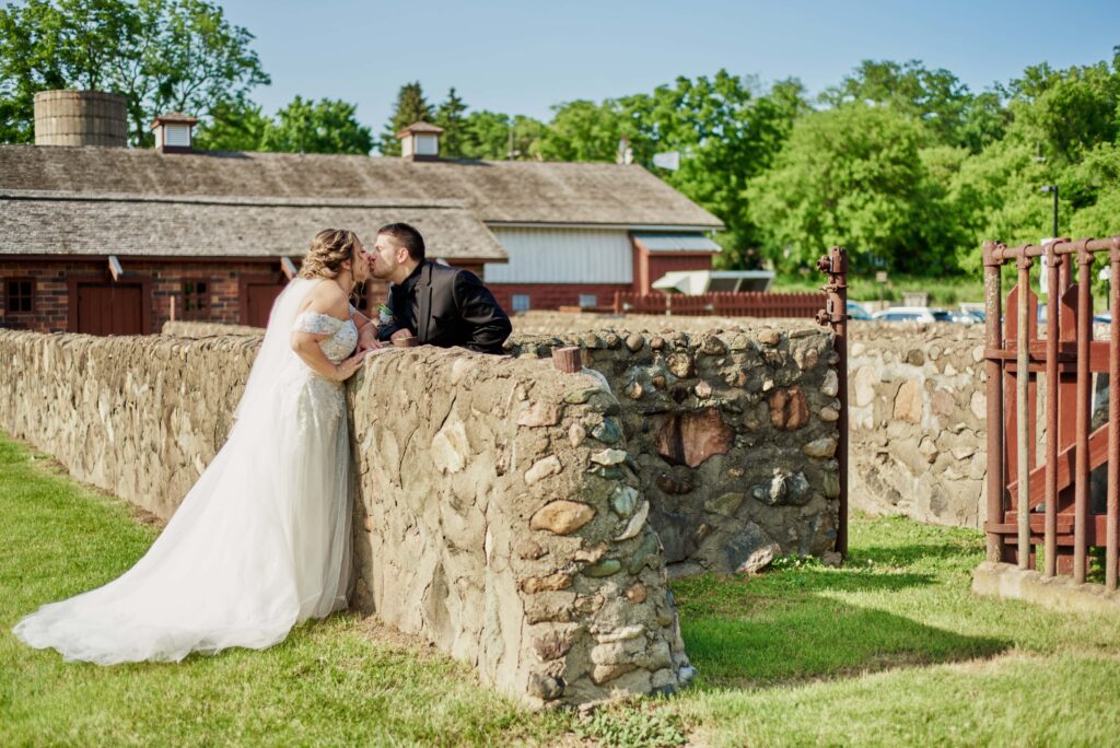 Bride and groom lean over a stone wall at Van Hoosen Farm in Rochester Hills, MI. Photo taken by Erika Black Photography