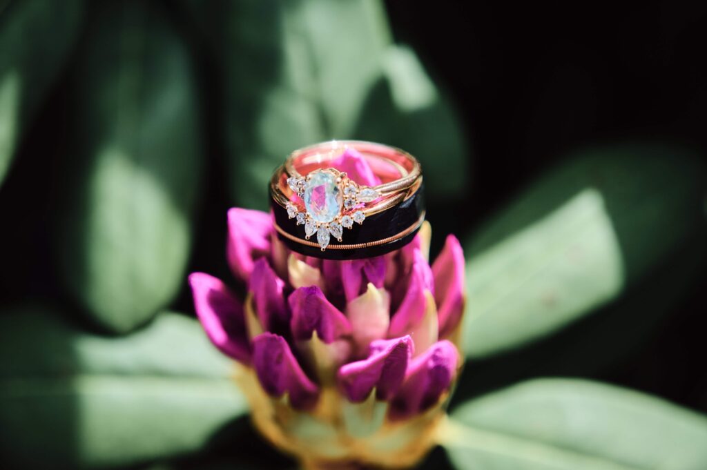 A wedding diamond ring and bands sit on top of a purple pink flower