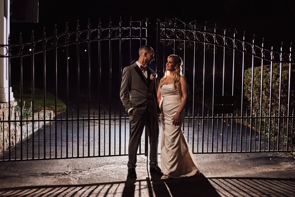 Bride and Groom stand together in front of the closed gate at Wellers in Saline, Michigan. Photo taken by 