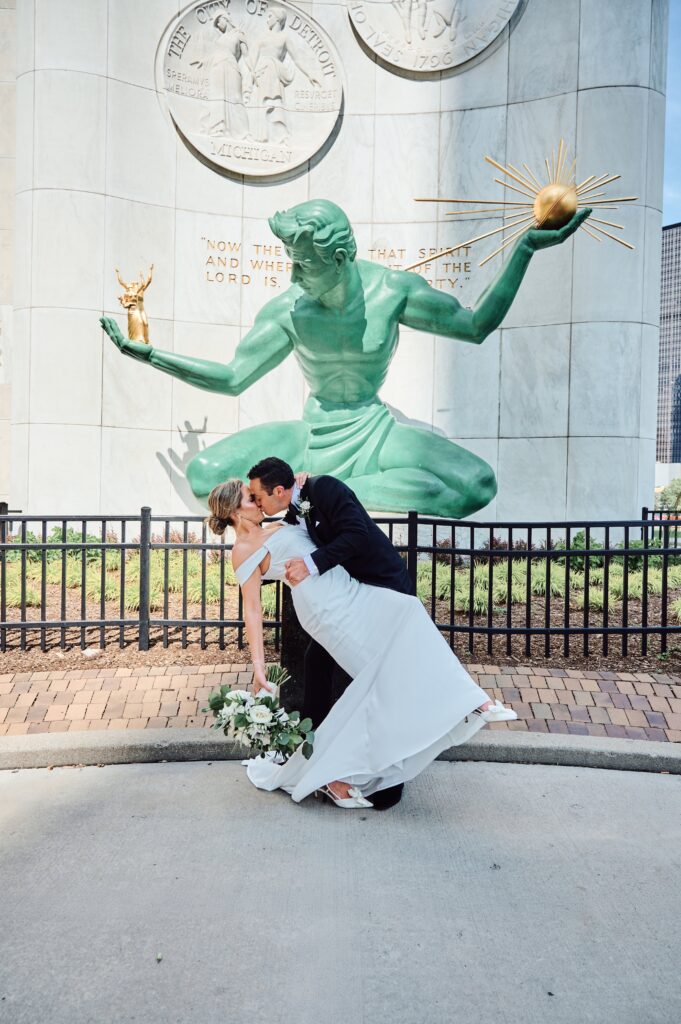 Groom dips and kisses the bride in front of the Spirit of Detroit in downtown Detroit, Michigan