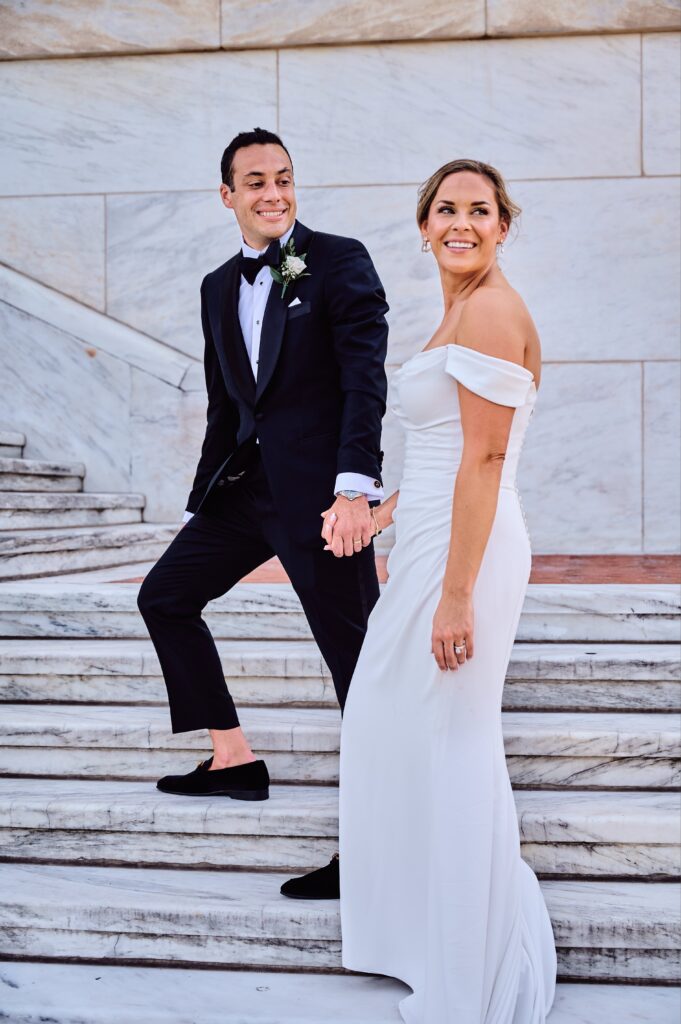 The groom guides the bride up the white marble steps of the Detroit Institute of Arts in Detroit, Michigan