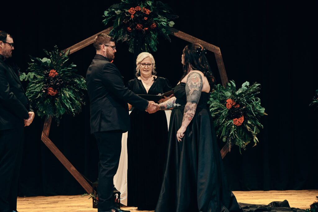 A bride and groom with their officiant on stage during their hand fasting ceremony