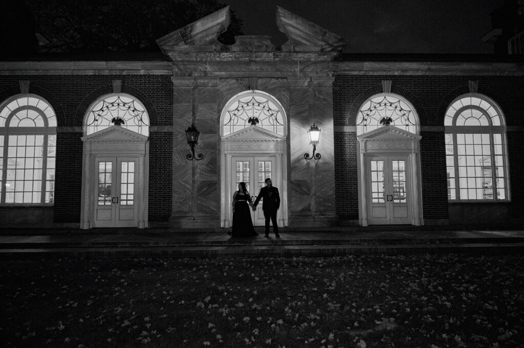 A bride and groom hold hands outside at night at the Henry Ford Museum