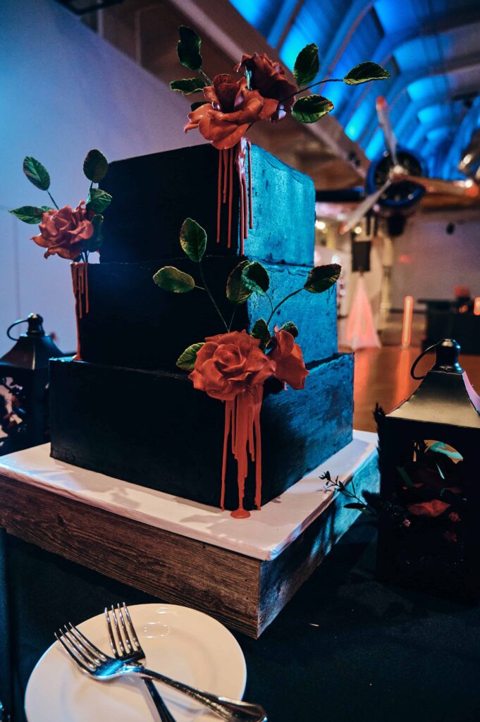 A black, square wedding cake with red roses and dripping red icing on the corners