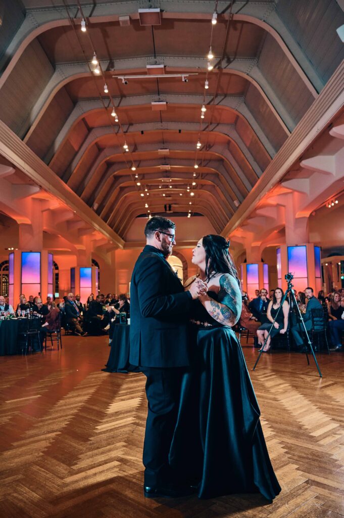 A bride in a black wedding dress and a groom in a black suit dance in front of their wedding guests at the Henry Ford Museum 