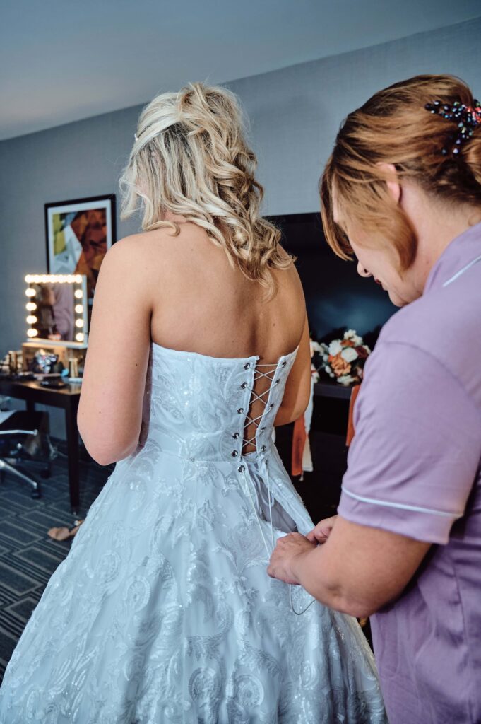Bride and mother of the bride doing up the back of the bride's dress at hotel in Lapeer, Michigan
