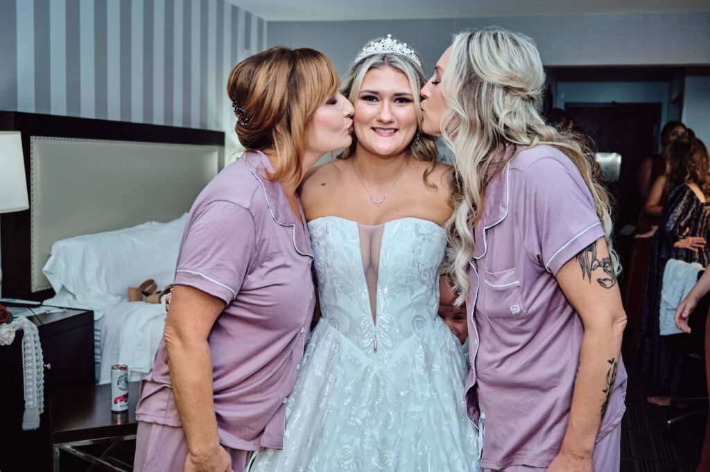 Mother of the bride and Step-mother of the bride kiss the bride on the cheeks in hotel in Lapeer, Michigan