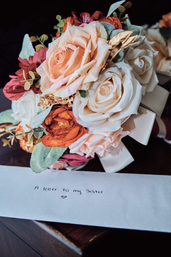 Pink, white, orange flower bouquet sitting next to a bride's thank you letter to her sister.