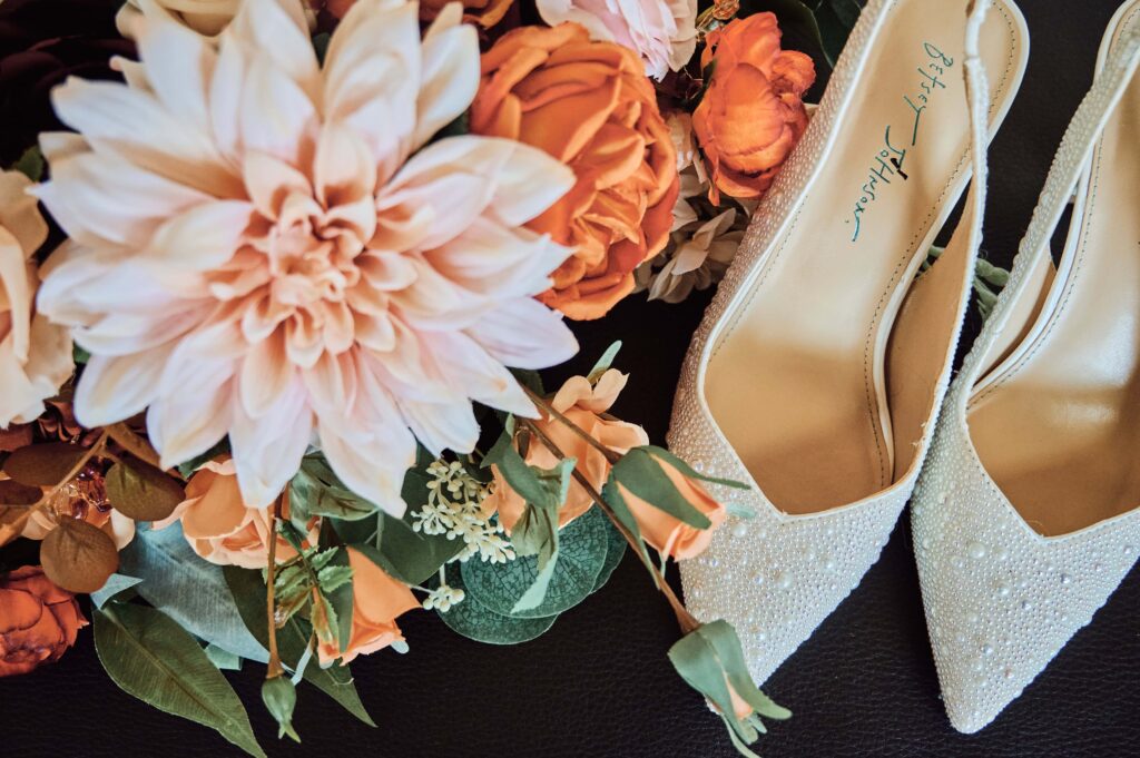 Pink and orange flower bridal bouquet next to white, beaded bridal shoes.