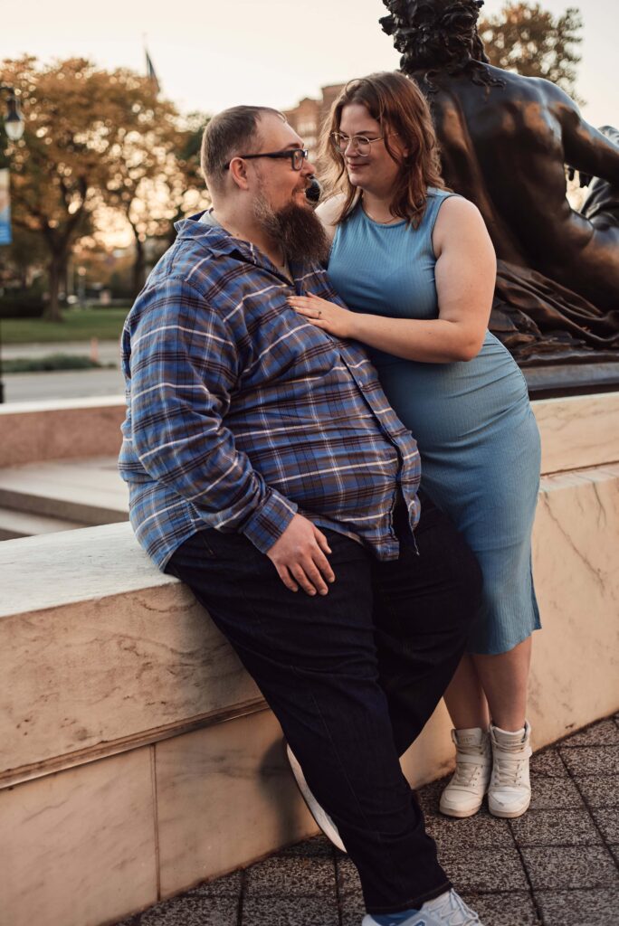 An engaged couple post on wall snuggled close to each other during their engagement session at sunset at the Detroit Institute of Arts