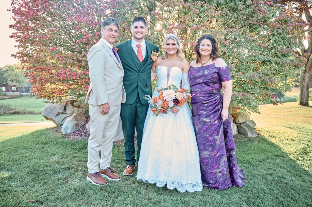 The bride and groom with the groom's parents standing at sunset at Lapeer Country Club