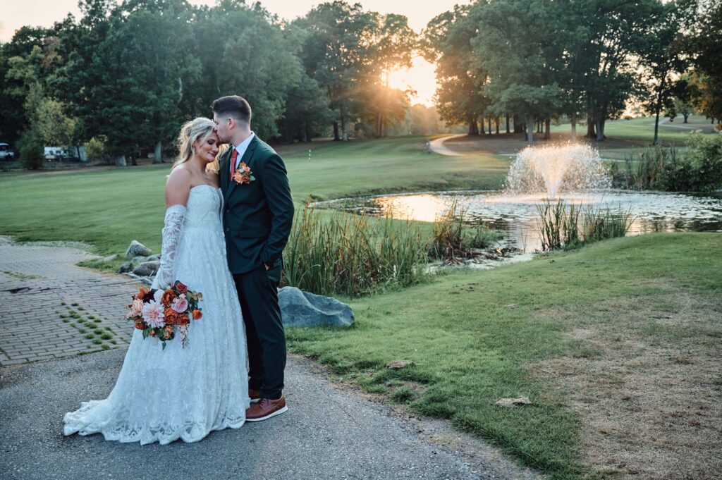 Groom kisses bride as she leans in near the fountain at Lapeer Country Club