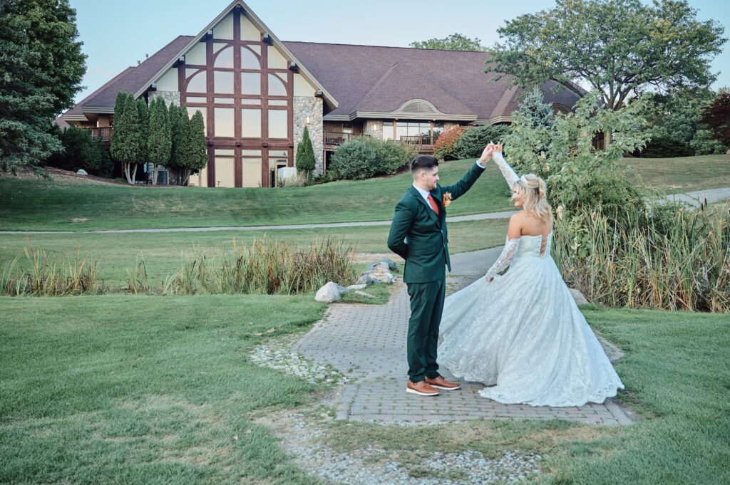 The groom twirls the bride in front of the club house at Lapeer Country Club