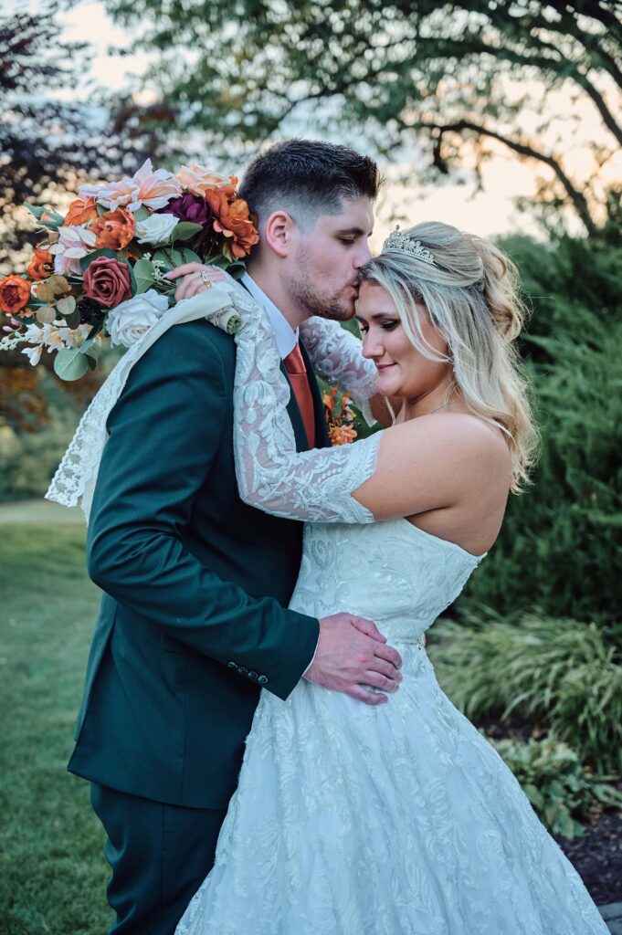 Groom kisses the bride on the head as the sun sets at Lapeer Country Club
