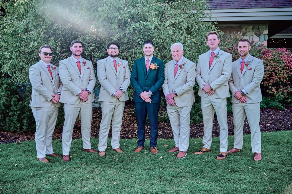 The groom in a forest green suit with his groomsmen in tan suits posing in a line at Lapeer Country Club