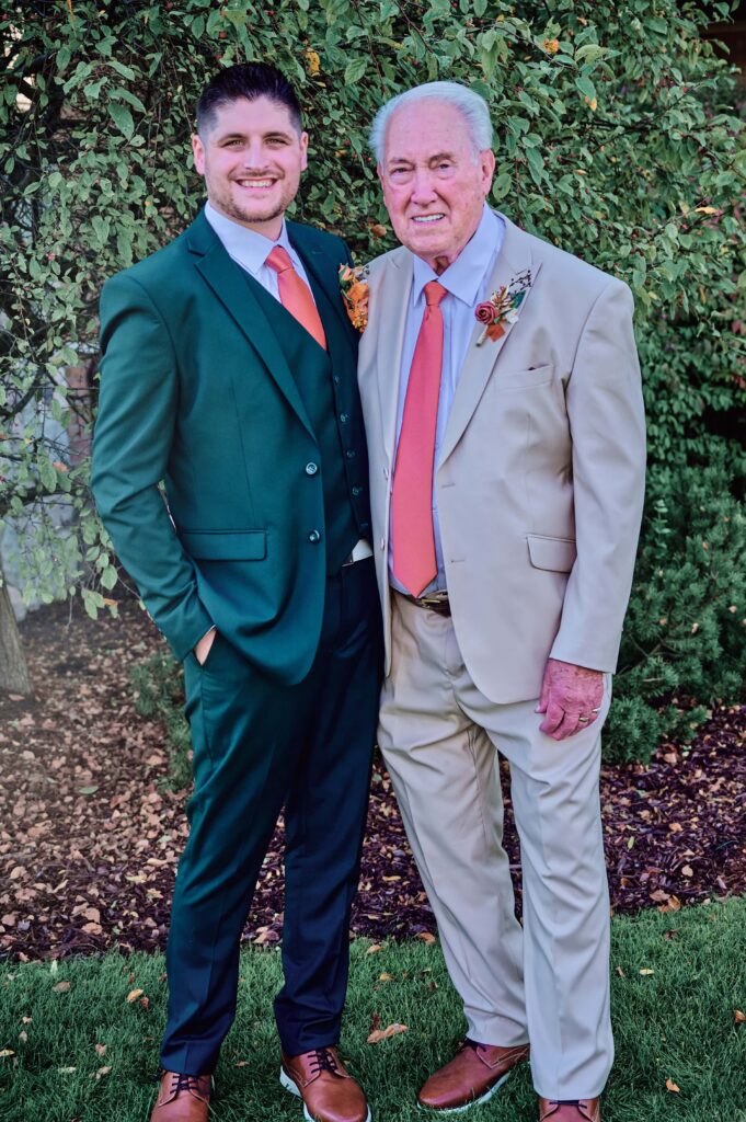 The groom in a forest green suit with his grandfather in a tan suit at Lapeer Country Club