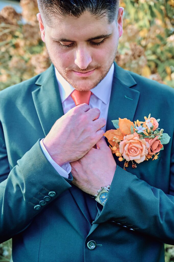 Groom in a forest green suit fixing his orange tie at Lapeer Country Club