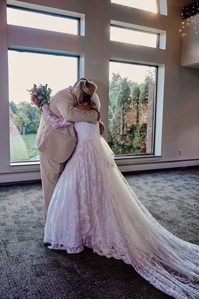 Father of the bride hugs his daughter, the bride, on her wedding day first look at Lapeer Country Club