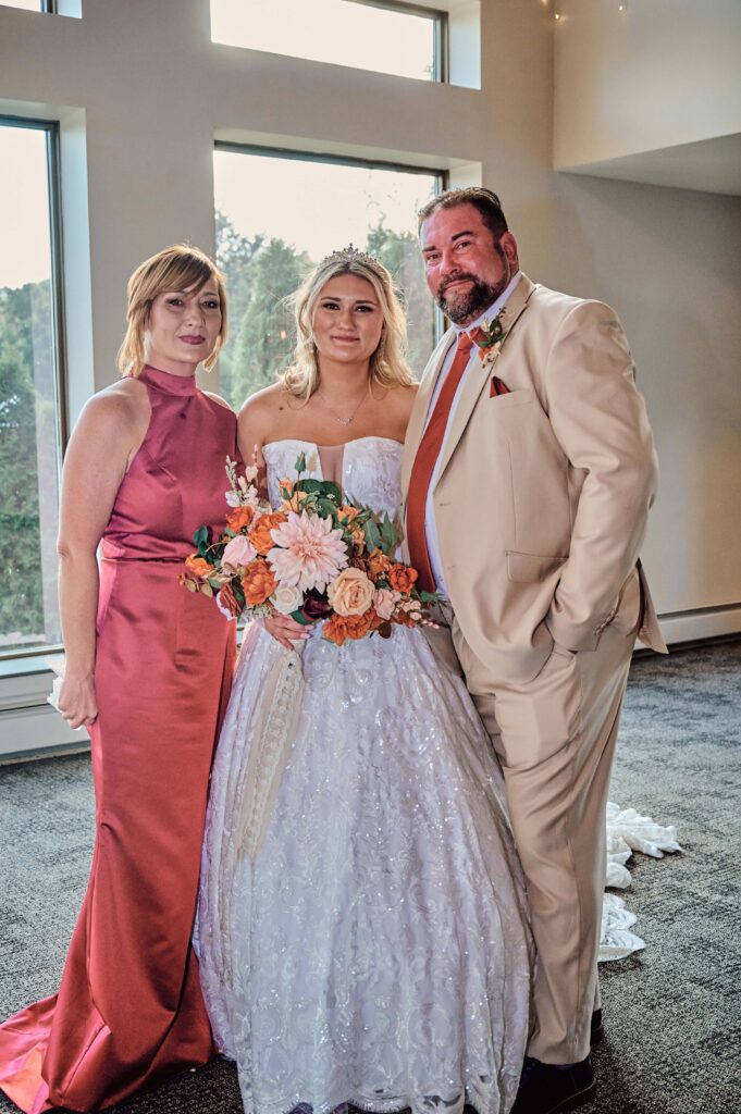 Mother of the bride, the bride, and father of the bride posing after the father and daughter first look at Lapeer Country Club
