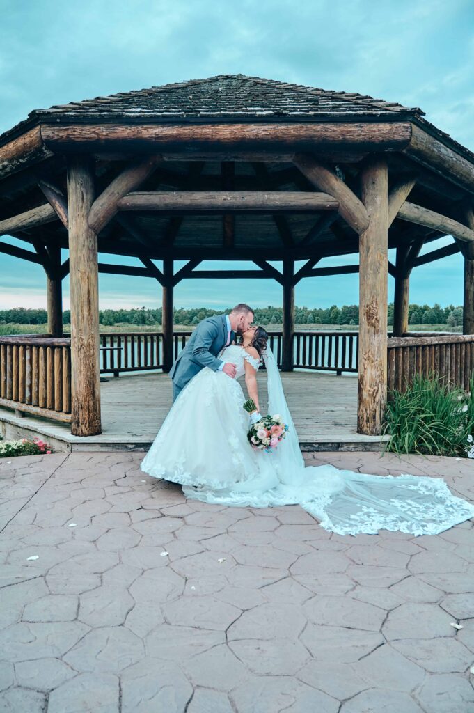 A groom dips the bride back in front of a large gazebo