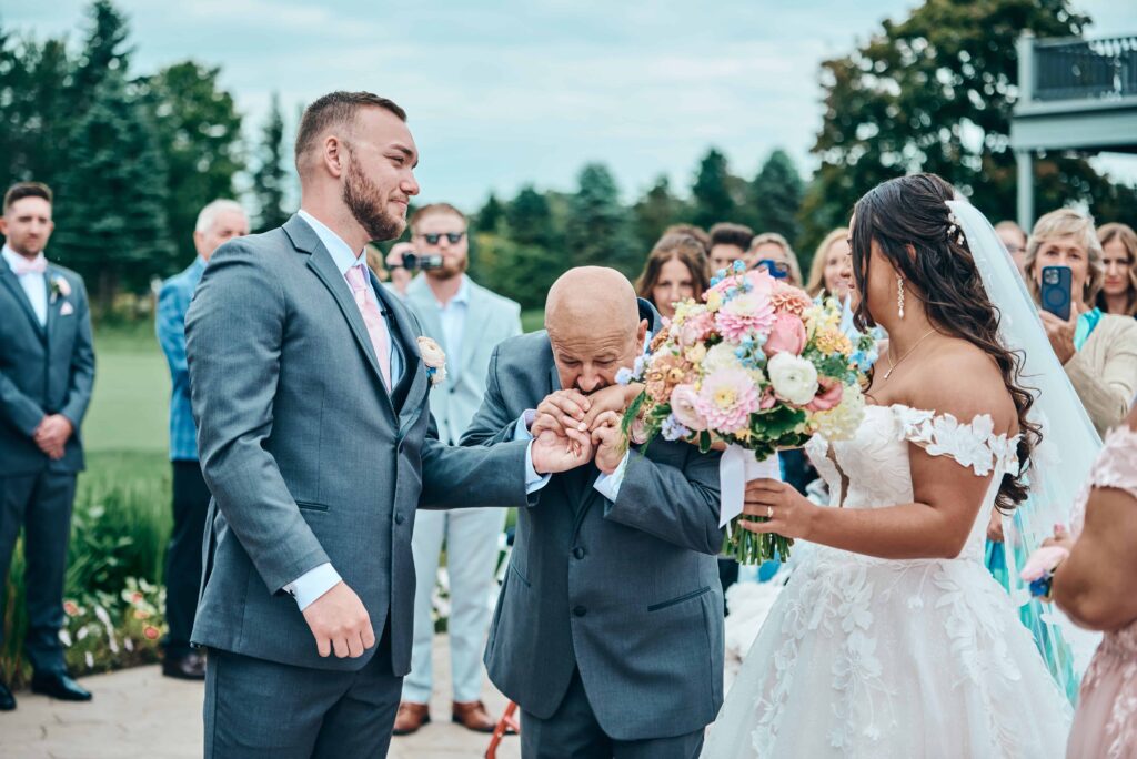 The father of the bride joins the groom and bride's hands together and kisses the hands for good luck right before they say their "I dos"