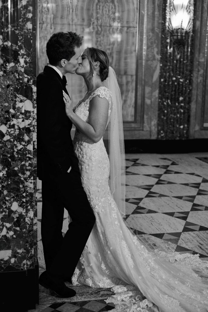 A bride and groom kiss in a hall surrounded by marble and art deco designed floor and walls
