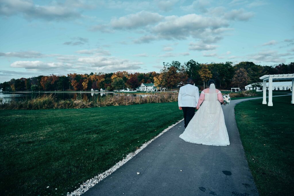 A bride and groom walk away along a path surrounded by a green lawn